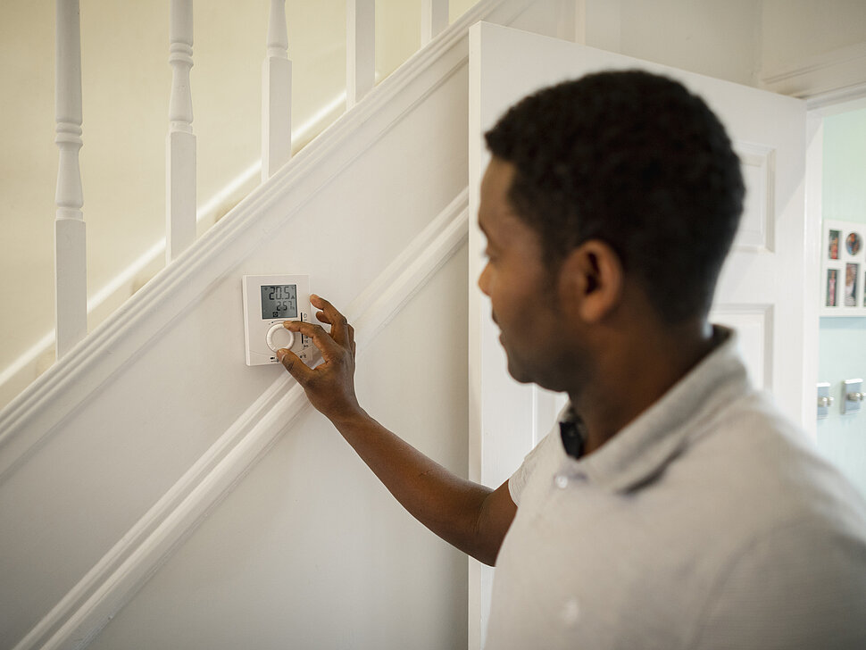 Menn dreht an einem Thermostat in seinem Haus